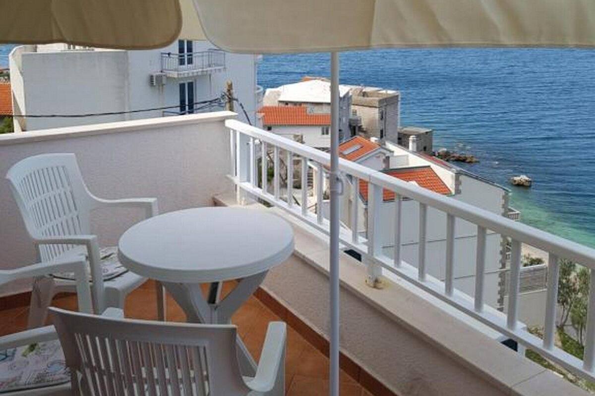A balcony with a table and chairs, overlooking a coastal area with buildings and the sea.