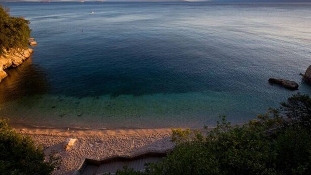 Un paysage côtier avec une eau limpide, une côte rocheuse et des reliefs visibles au loin.