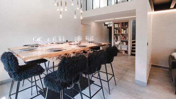 Een moderne eethoek met een lange houten tafel, zwarte, pluizige stoelen en hangende hanglampen.