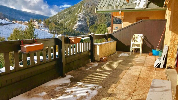 Ein Balkon mit Blick auf einen verschneiten Berg, einem Holzzaun und einem Stuhl.