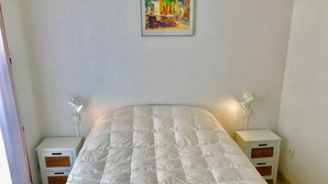 Ein ordentlich bezogenes Bett mit einer weißen Decke, zwei Nachttische mit Lampen, ein kleines Bild an der Wand und ein gemustertes Teppich.