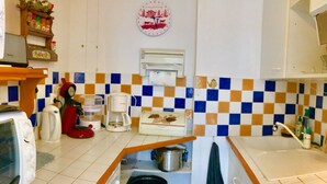 Eine kleine Küche mit Mikrowelle, Kaffeemaschine und Wasserkocher. Rückwand mit Schachbrettmuster und eine Uhr an der Wand.