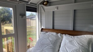 Ein Schlafzimmer mit einem Holzkopfteil, weißer Bettwäsche und Blick auf einen Garten durch eine Schiebeglastür.