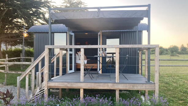 Eine Holzterrasse mit Tisch, Stühlen, einem Bett und einem überdachten Bereich.