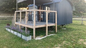 Eine Holzterrasse mit Glasverkleidung, einer Metallkonstruktion und einem kleinen Garten mit Blumen.