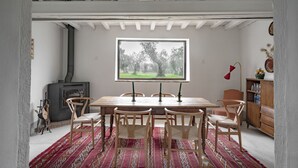 A dining area with a wooden table and chairs, a window with a view of trees, a fireplace, and a bookshelf.