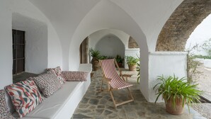 A covered outdoor seating area with a stone floor, white walls, and arches.