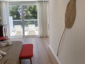 A bedroom with a bed, a bench, a wall-mounted decorative item, and a view of a balcony with outdoor furniture.