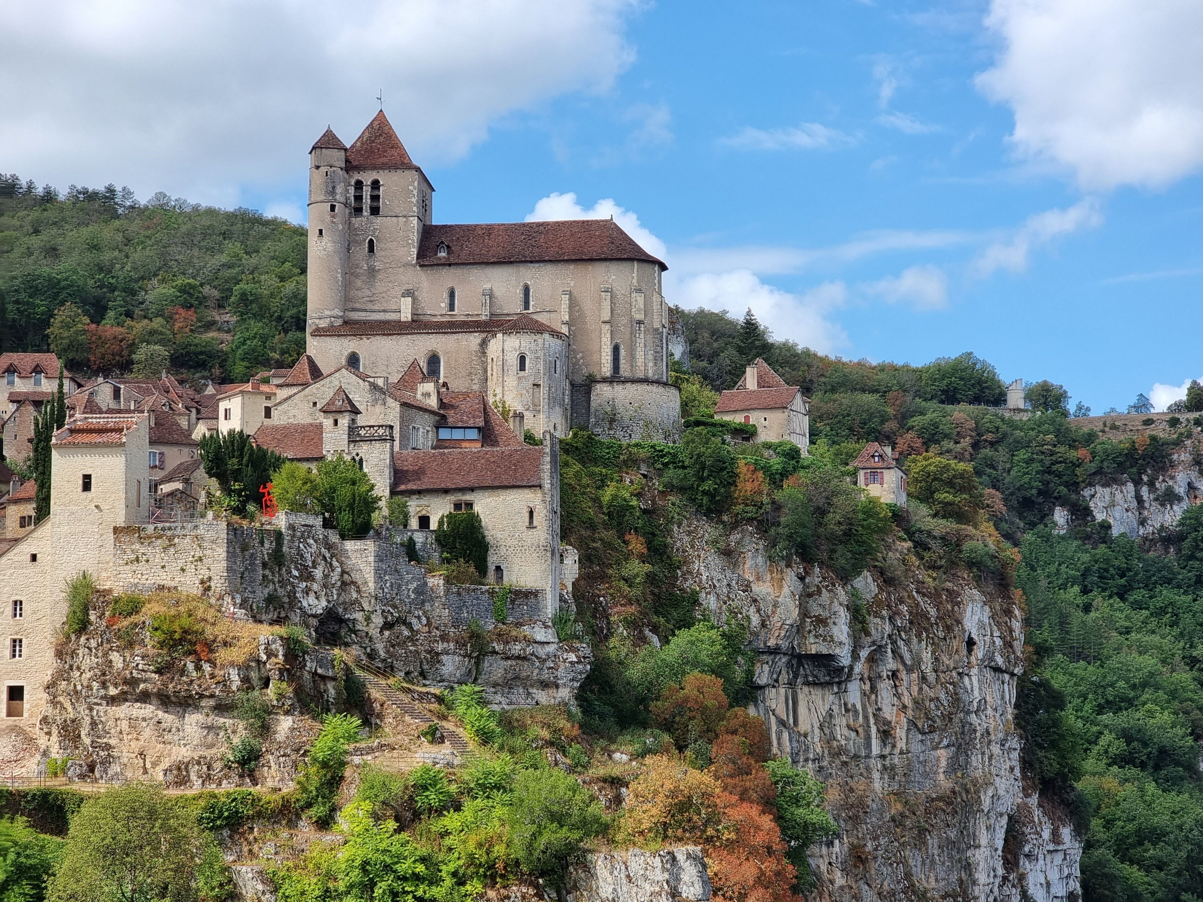 A historic castle with a prominent tower, situated on a rocky hill surrounded by lush greenery.