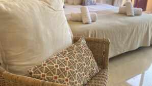 Une chambre d’hôtel avec un grand lit, deux oreillers, un fauteuil en osier et une table de chevet avec une lampe.