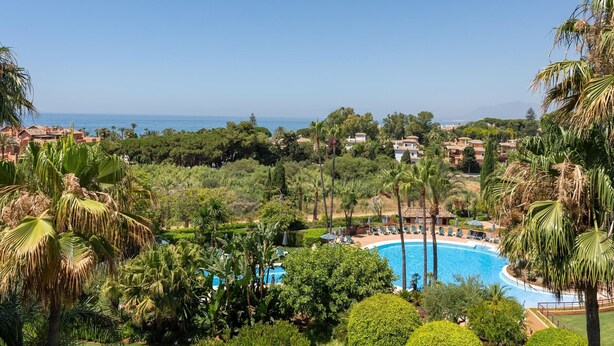 Un complexe hôtelier doté d’une piscine entourée d’une végétation luxuriante et de palmiers, offrant une vue sur la côte.