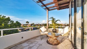 A balcony with wicker chairs, a glass table, and a potted plant. - Villa Kalita (Seminyak)