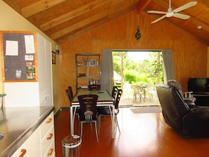 A cozy cabin interior with a dining area, a living room with a sofa and TV, and a balcony with a view of greenery. - Mill Bay Charmer (Mangonui)