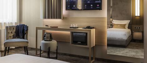 Habitación de hotel con cama, escritorio con televisor, silla y una mesita con un bolso.