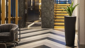 Un hall d’entrée moderne avec un sol à motifs en chevrons noir et blanc, une grande plante en pot et un ascenseur élégant.