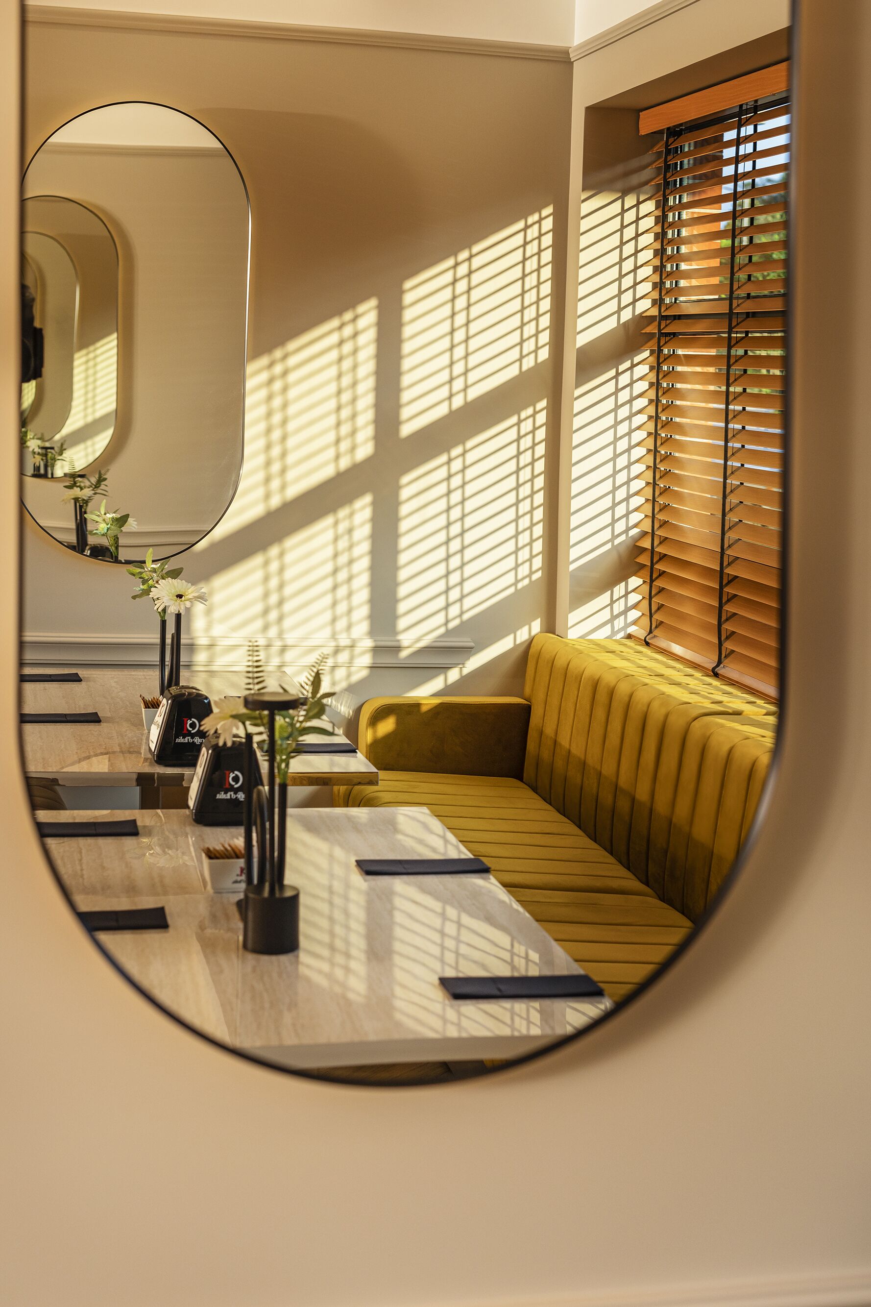 Un interior moderno con un sofá amarillo, un espejo redondo y una mesa de madera con un florero y un reloj.