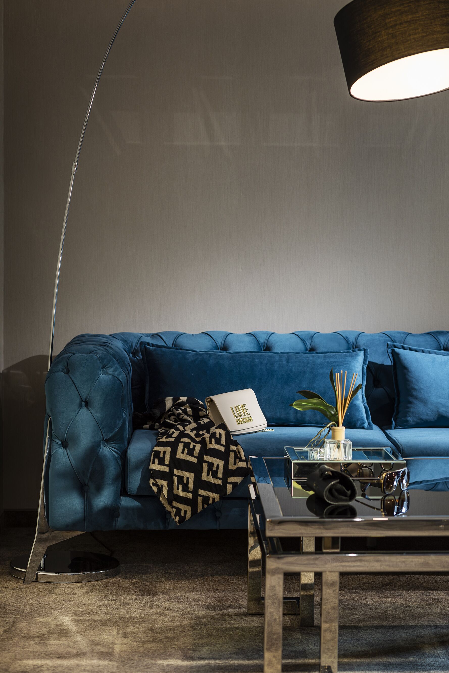 Ein blaues, gepolstertes Sofa mit einer gemusterten Decke, einem Glastisch und einer Stehlampe.