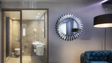 Un baño moderno con cabina de ducha de vidrio, un espejo redondo y un sofá azul en una sala de estar.
