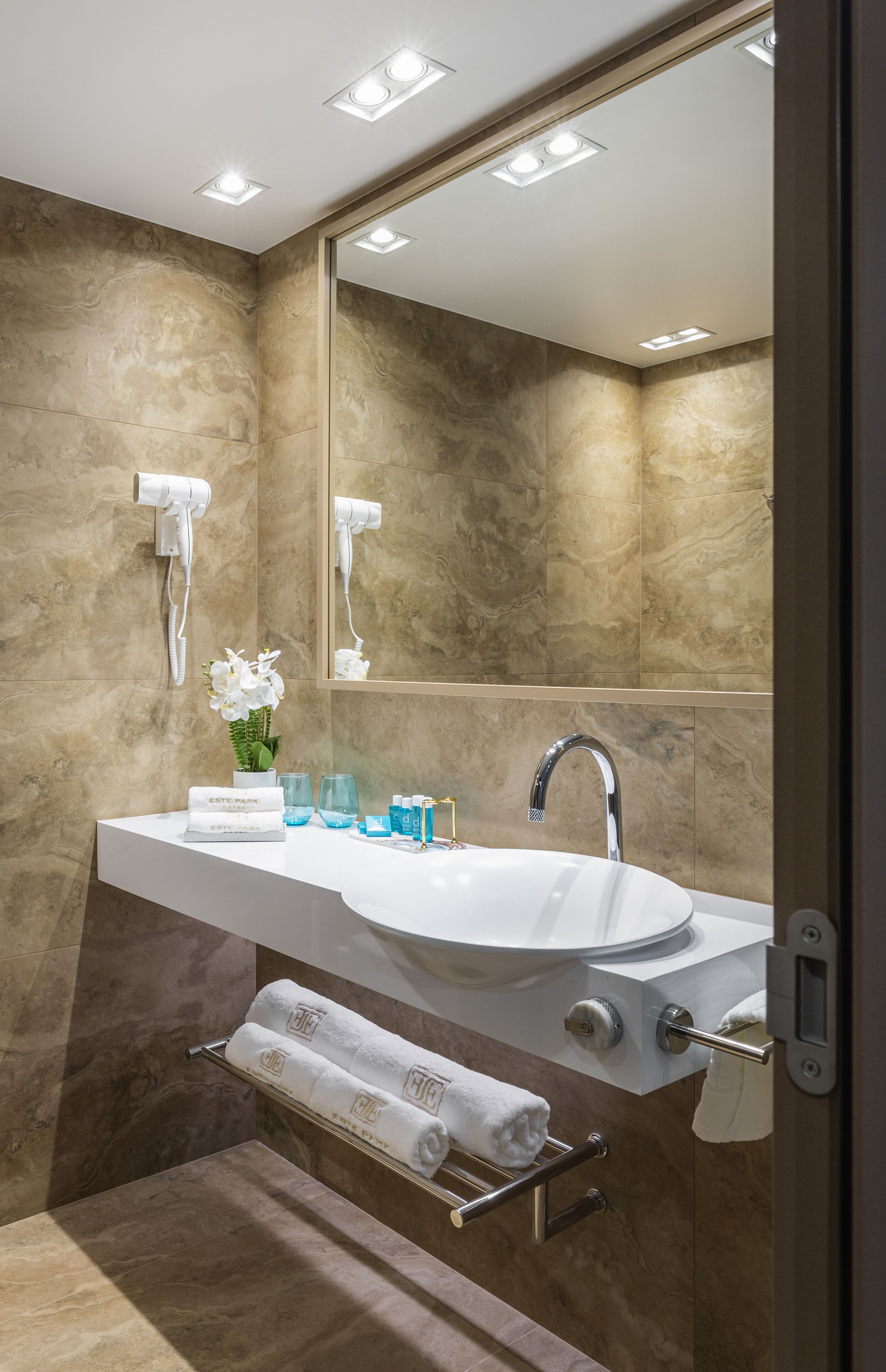 Un baño moderno con un espejo grande, un lavamanos blanco y dos toalleros.