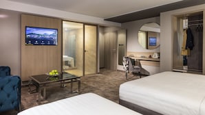 Une chambre d’hôtel avec deux lits, un bureau, une chaise, une télévision, une armoire et un miroir.