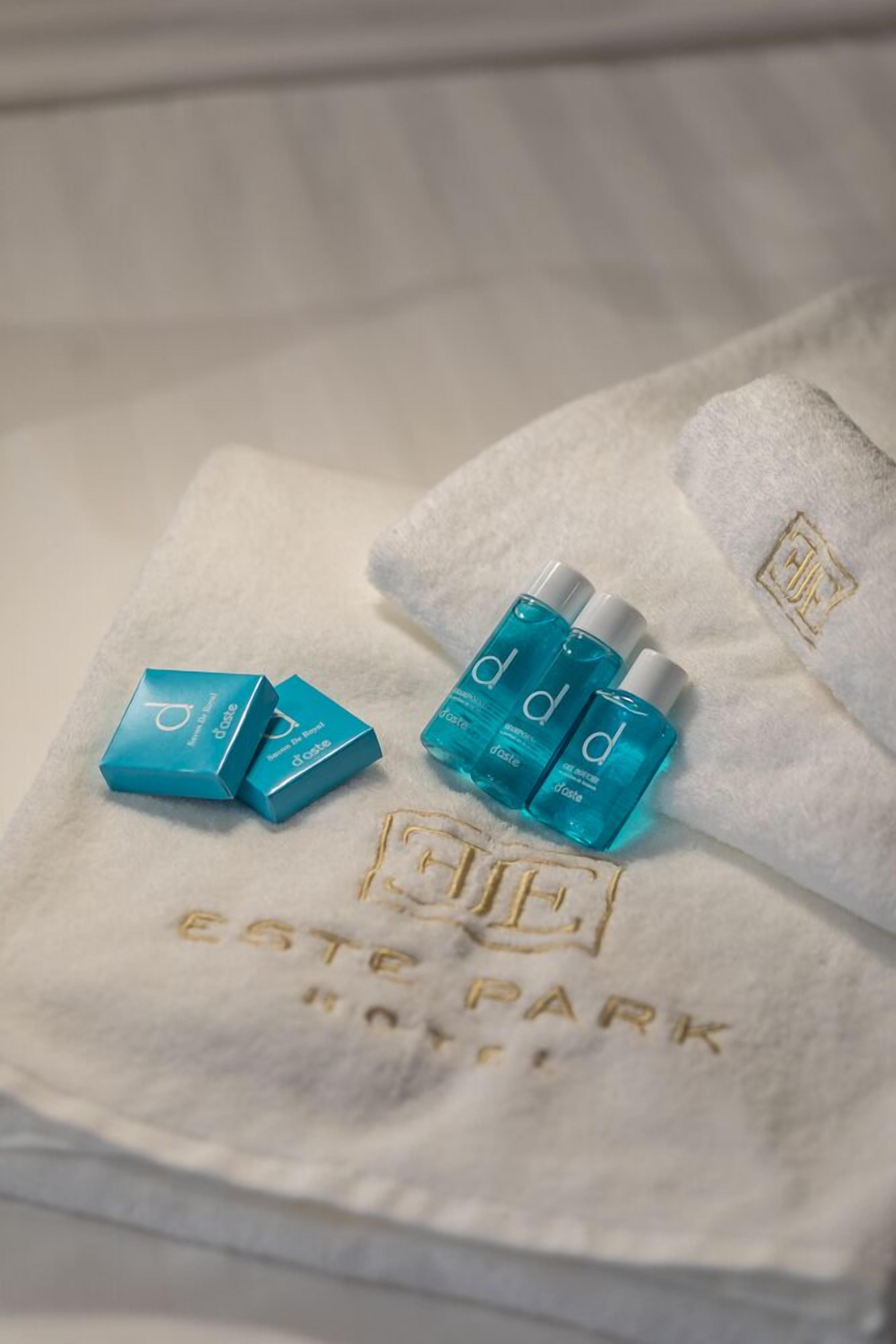 A white towel with embossed text reading "ESTE PARK" and three blue bottles with white caps.