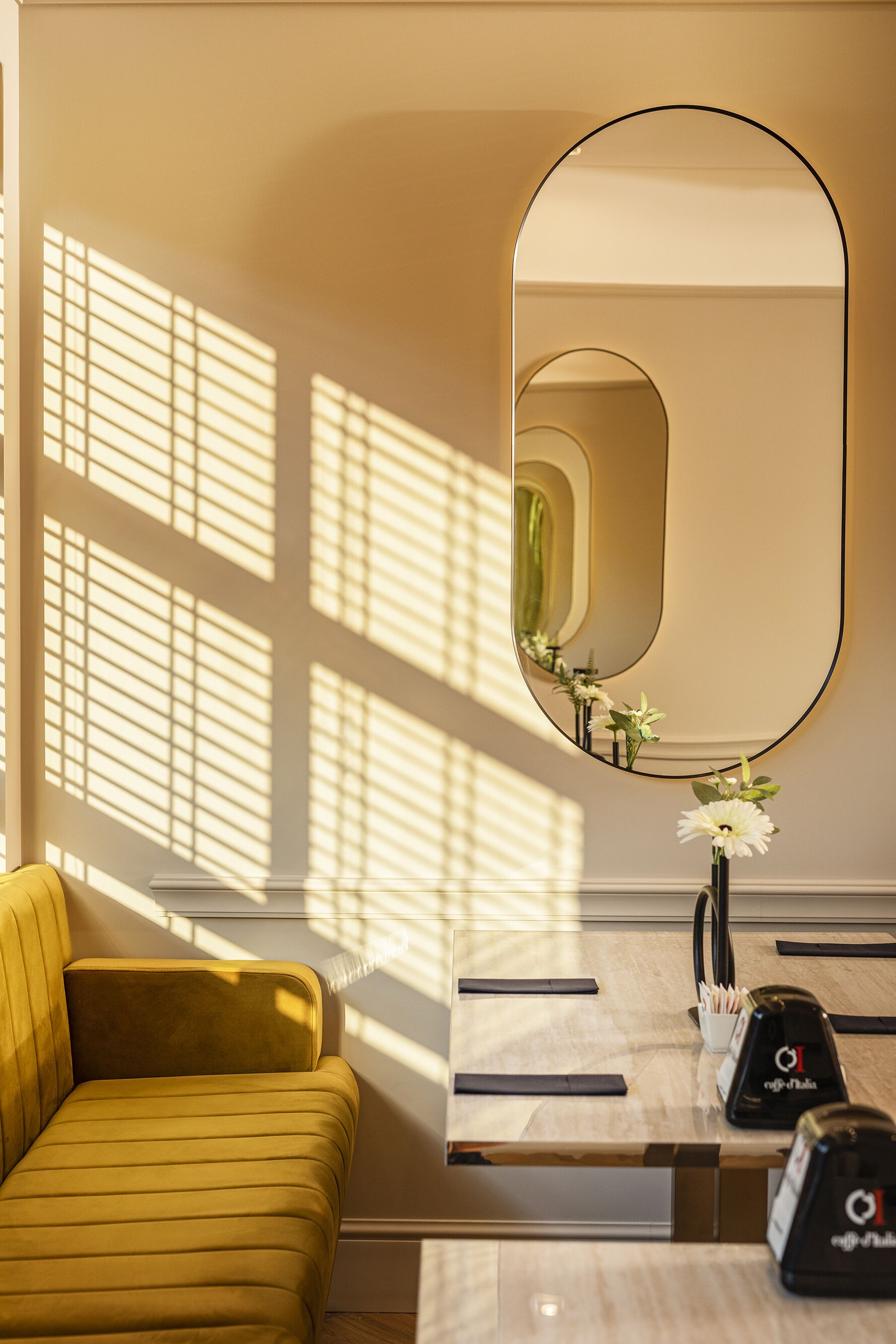 A modern room with a yellow sofa, a large mirror, and a small table with a vase of flowers.