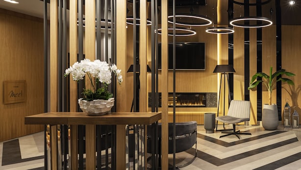 Un intérieur moderne avec un comptoir d’accueil en bois, un fauteuil noir, une plante en pot et une cheminée.