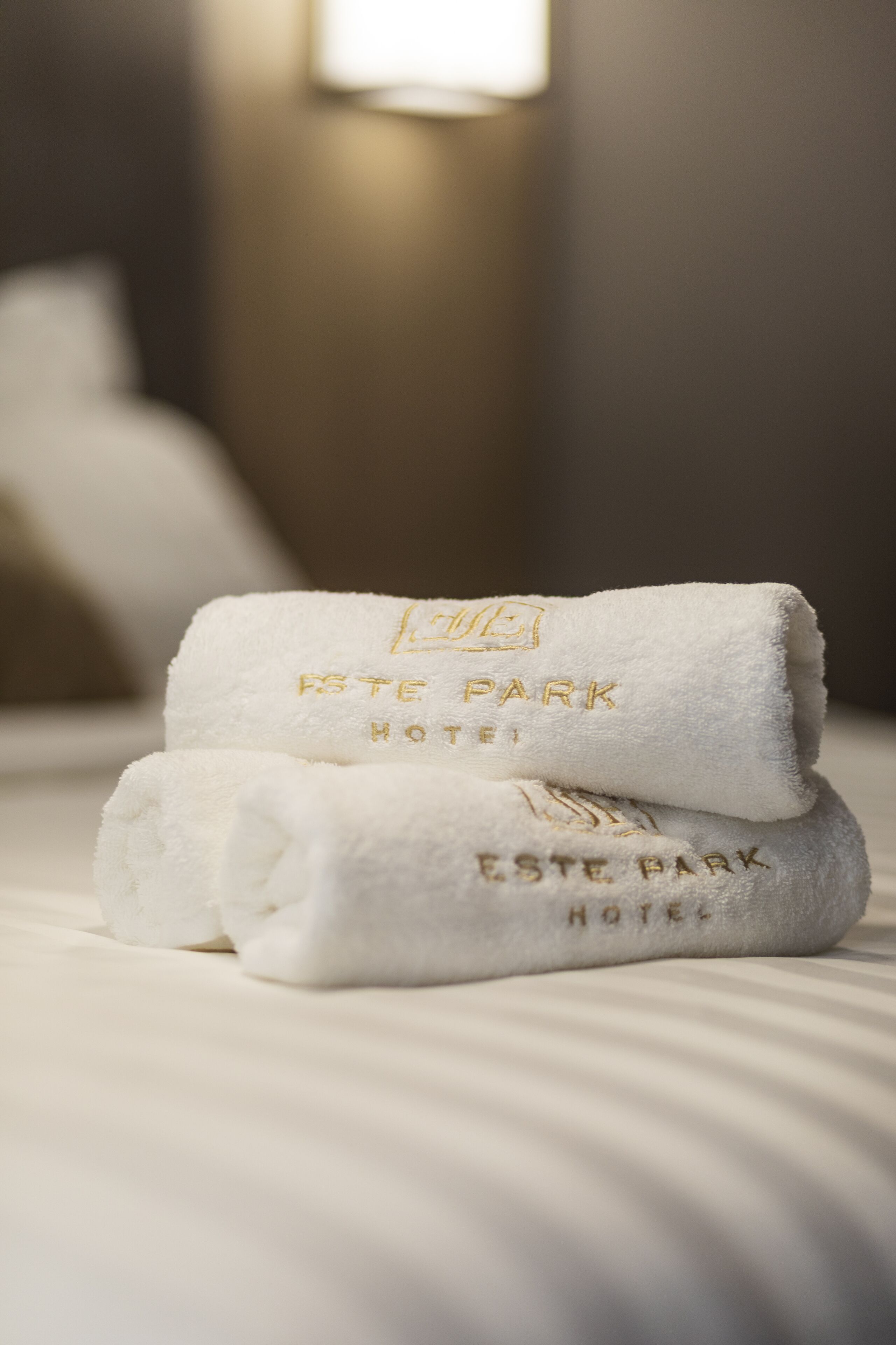 Two folded white towels with "Este Park Hotel" embossed on them, placed on a bed.