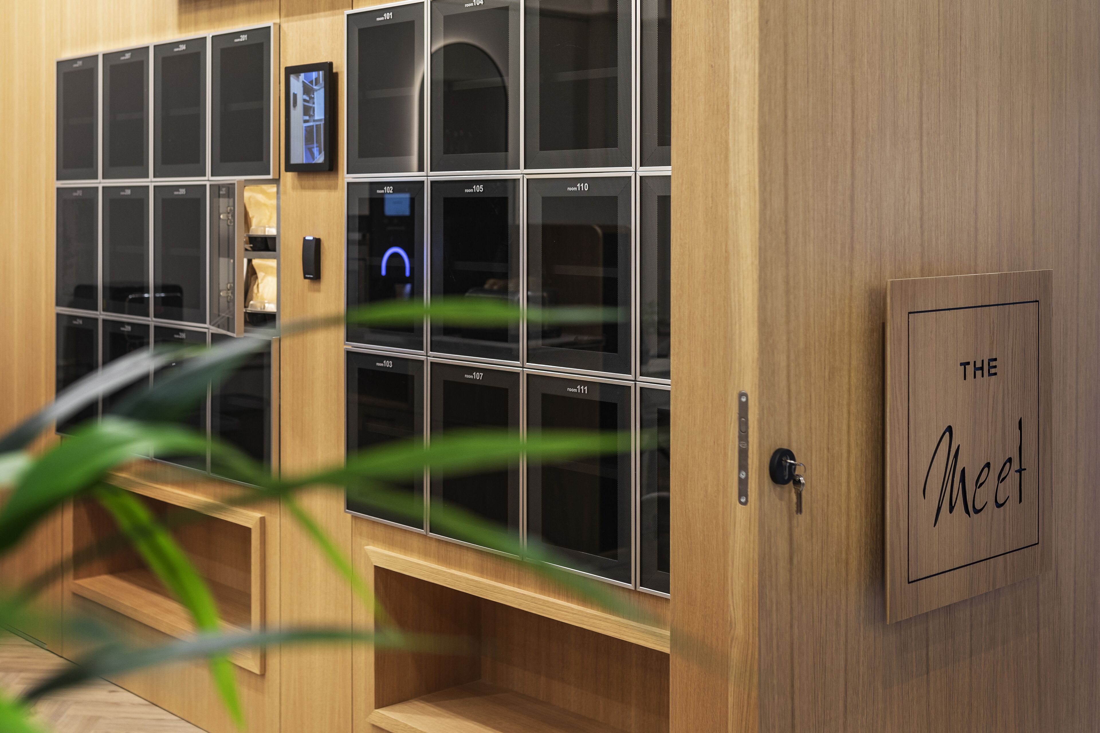 Habitación de hotel con detalles de madera, una cerradura digital y un cartel que dice 'THE Meet'.