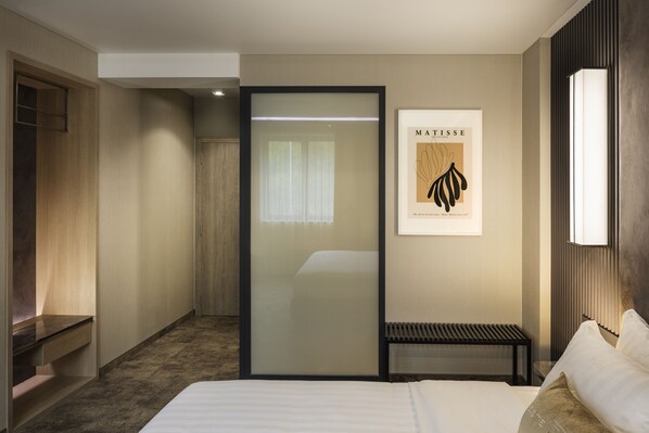 A hotel room with a bed, a bench, a wardrobe, and a framed artwork on the wall.