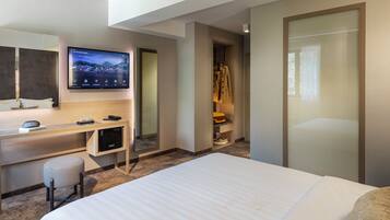 Habitación de hotel moderna con una cama grande, un escritorio con ordenador, un televisor de pantalla plana y un vestidor.