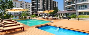 Une piscine entourée de bâtiments modernes, avec des chaises longues et des parasols.