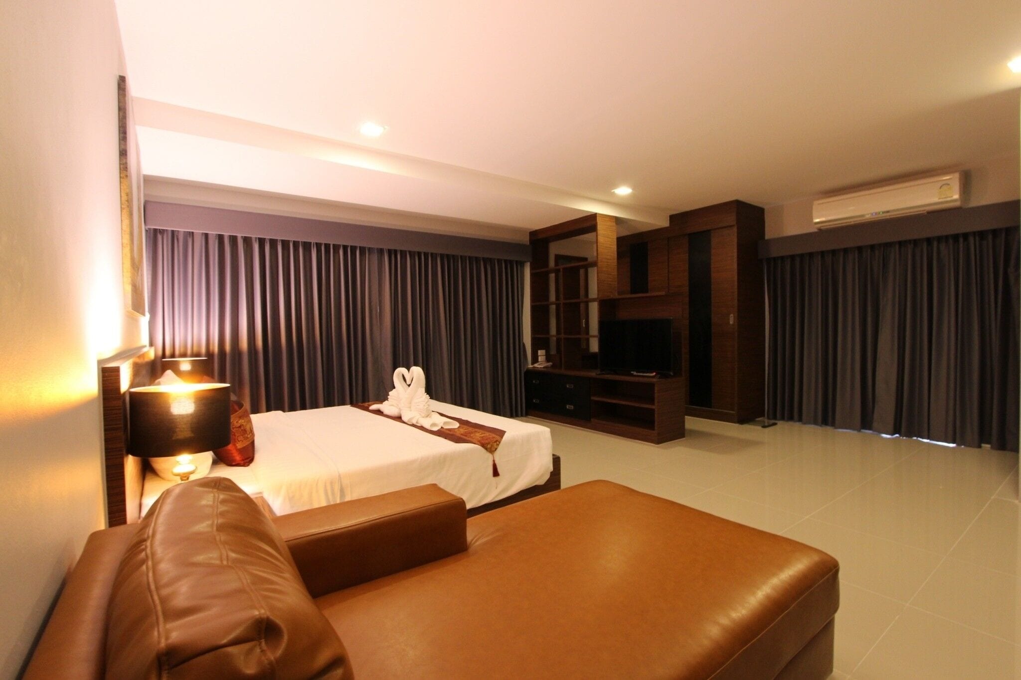 A hotel room with a bed, a sofa, a TV, and a minibar.