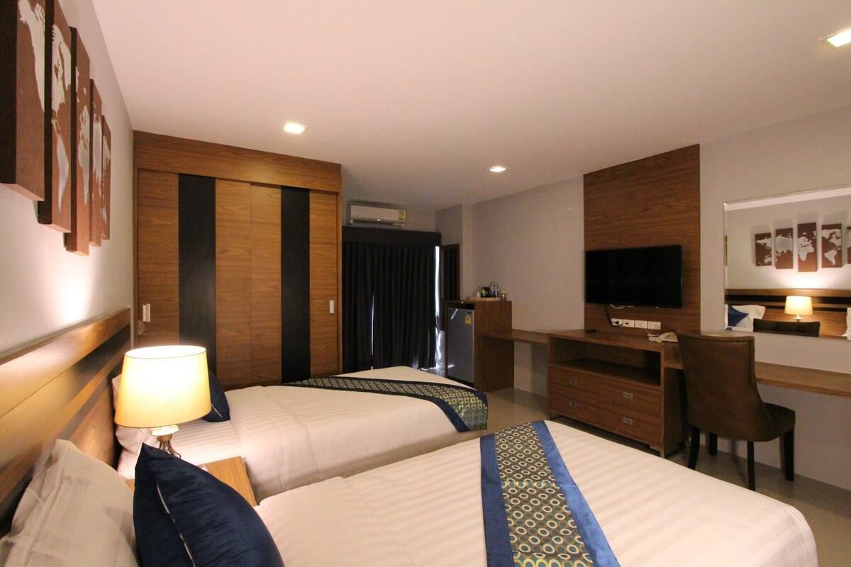 Habitación de hotel con dos camas, un escritorio, una televisión y un aire acondicionado.
