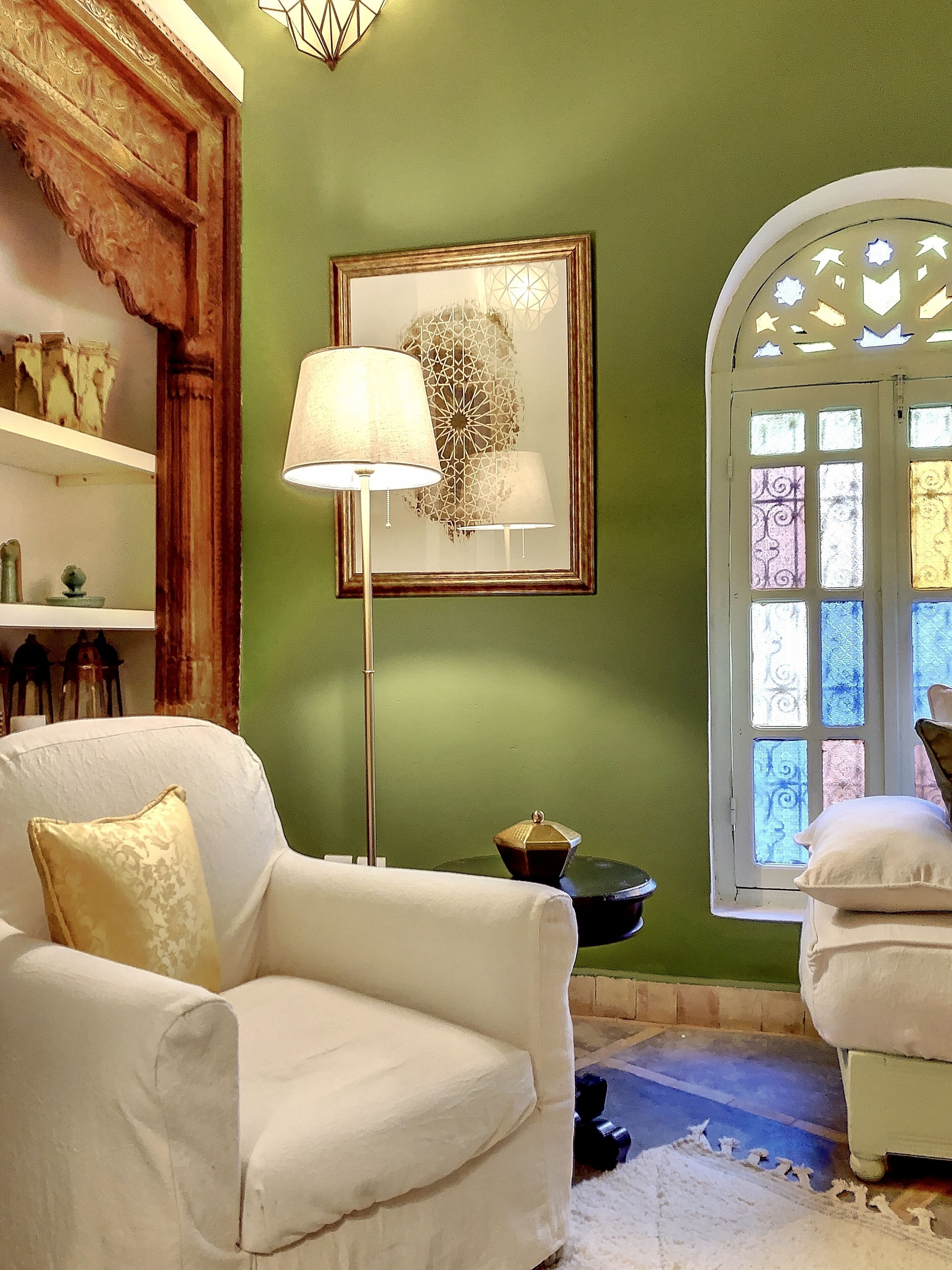 Une pièce avec un mur vert, un fauteuil blanc, un lampadaire et une œuvre d’art encadrée.