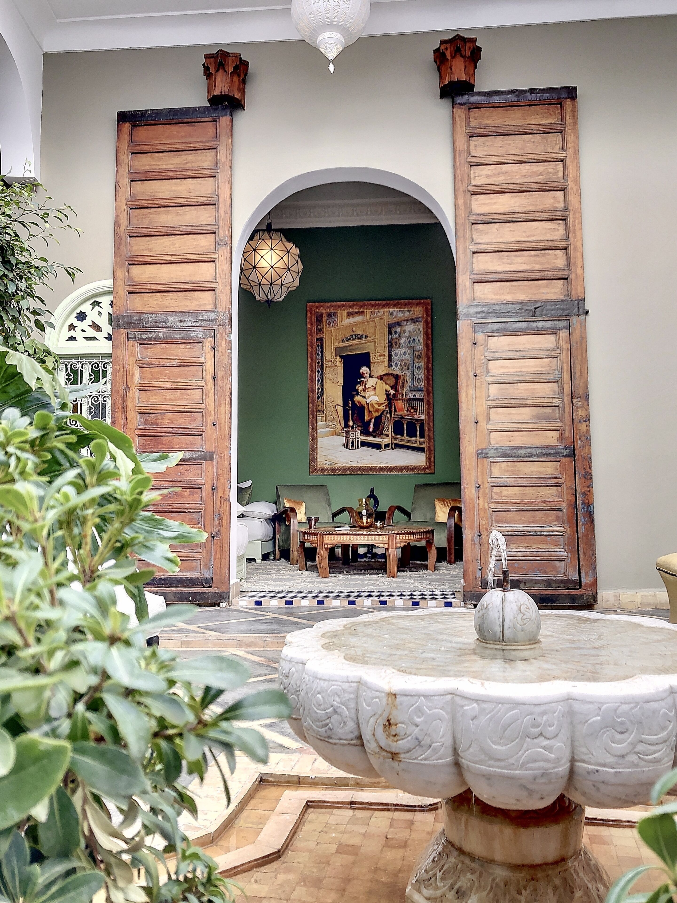 Une pièce dotée d’une grande porte en bois, d’une fontaine ronde en marbre et d’un tableau accroché au mur.
