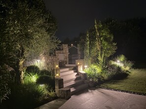 A stone staircase leading to a gated entrance, surrounded by illuminated plants and trees. - Villa Gelso (Soiano del Lago)