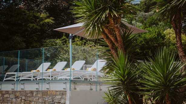 A poolside area with white lounge chairs and a glass railing.