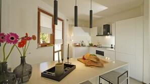 A modern kitchen with white cabinets, a central island, pendant lights, and a window with a view of greenery.