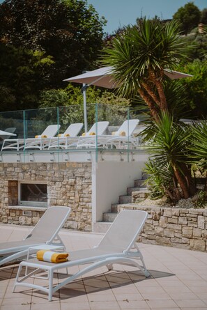 A pool area with lounge chairs, a glass balustrade, and a stone wall.