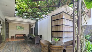 A wooden deck with wicker furniture, a bookshelf, and a hanging plant. - Palette near Legian Beach formerly Argya Santi Suites And Villas (Legian)