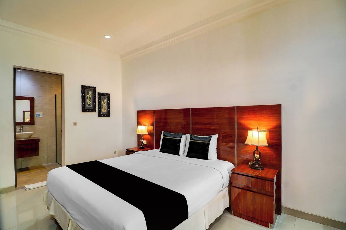 Ein Hotelzimmer mit einem großen Bett, Nachttischlampen, einem Holzkopfteil, einem kleinen Nachttisch und einem Spiegel.