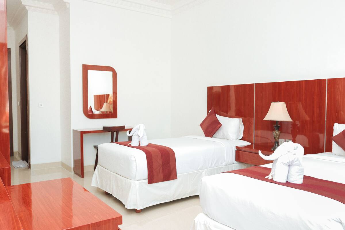 Ein Hotelzimmer mit zwei Betten, einem hölzernen Kopfteil, einem Spiegel, einem Schreibtisch und einer Lampe.