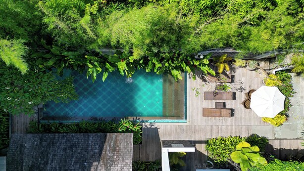 An aerial view of a modern pool area with a wooden deck, lounge chairs, and lush greenery. - Palette near Legian Beach formerly Argya Santi Suites And Villas (Legian)