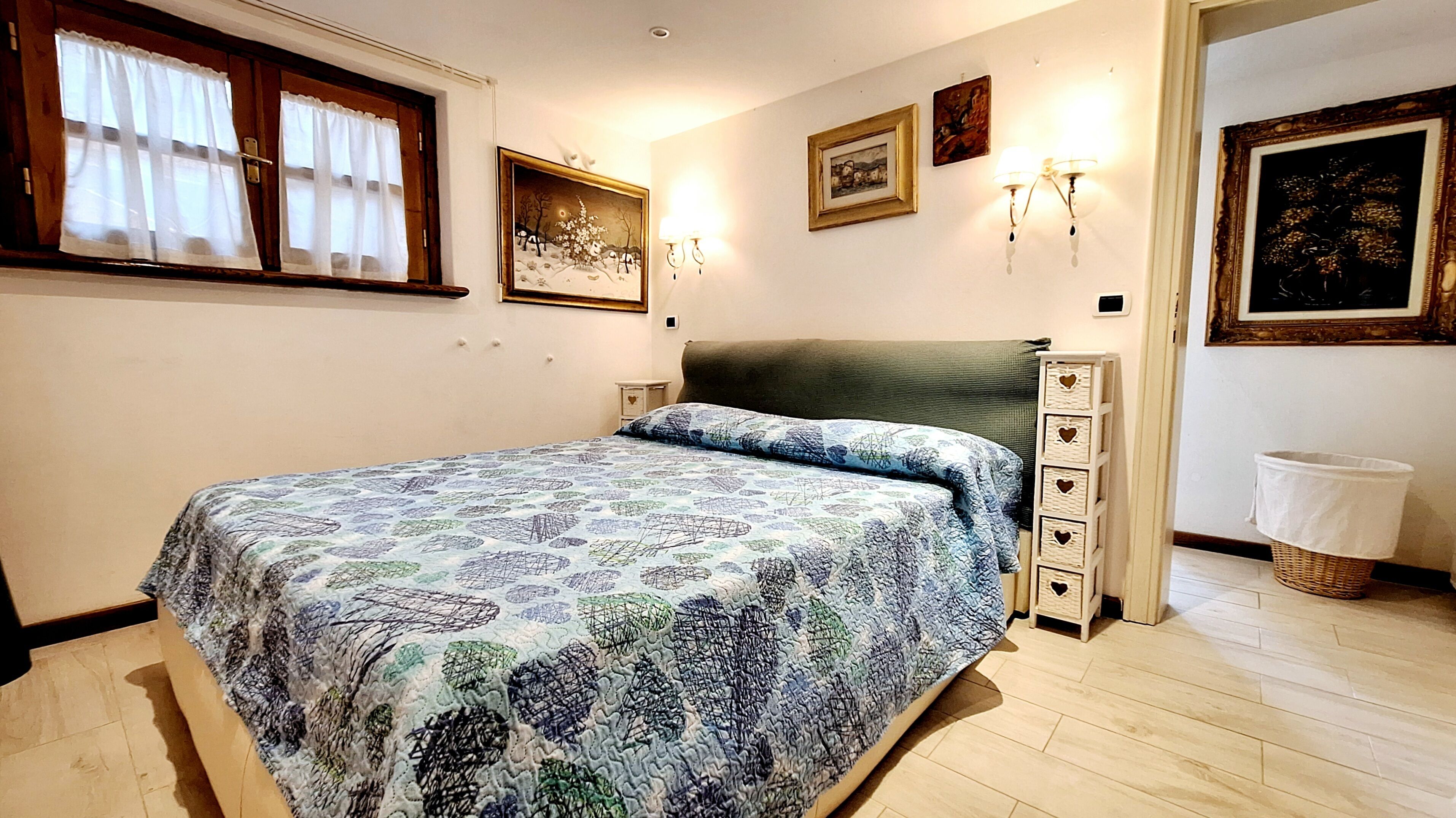 Een slaapkamer met een bed, een nachtkastje, een dressoir en een raam met gordijnen.