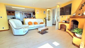 Een woonkamer met een witte bank, een houten salontafel en een open haard.