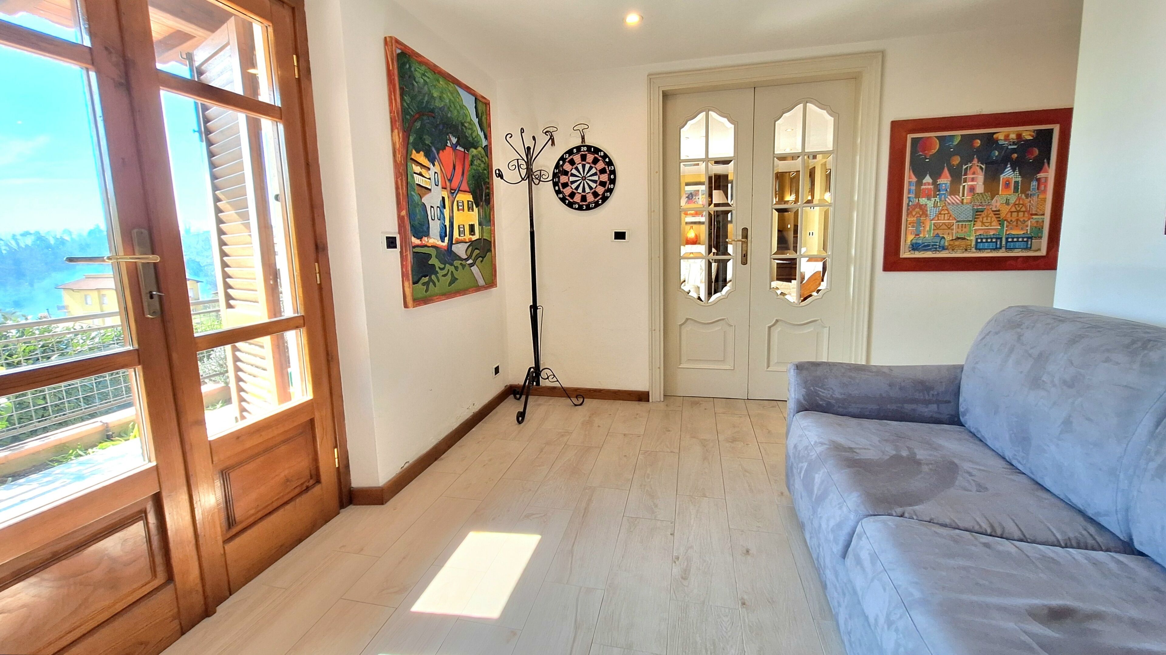 Une pièce avec un canapé gris, un plancher en bois, un jeu de fléchettes et un tableau accroché au mur.