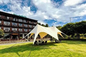 Un hotel con una gran estructura tipo tienda de campaña blanca en el patio, un edificio de varios pisos con balcones y un cielo despejado.