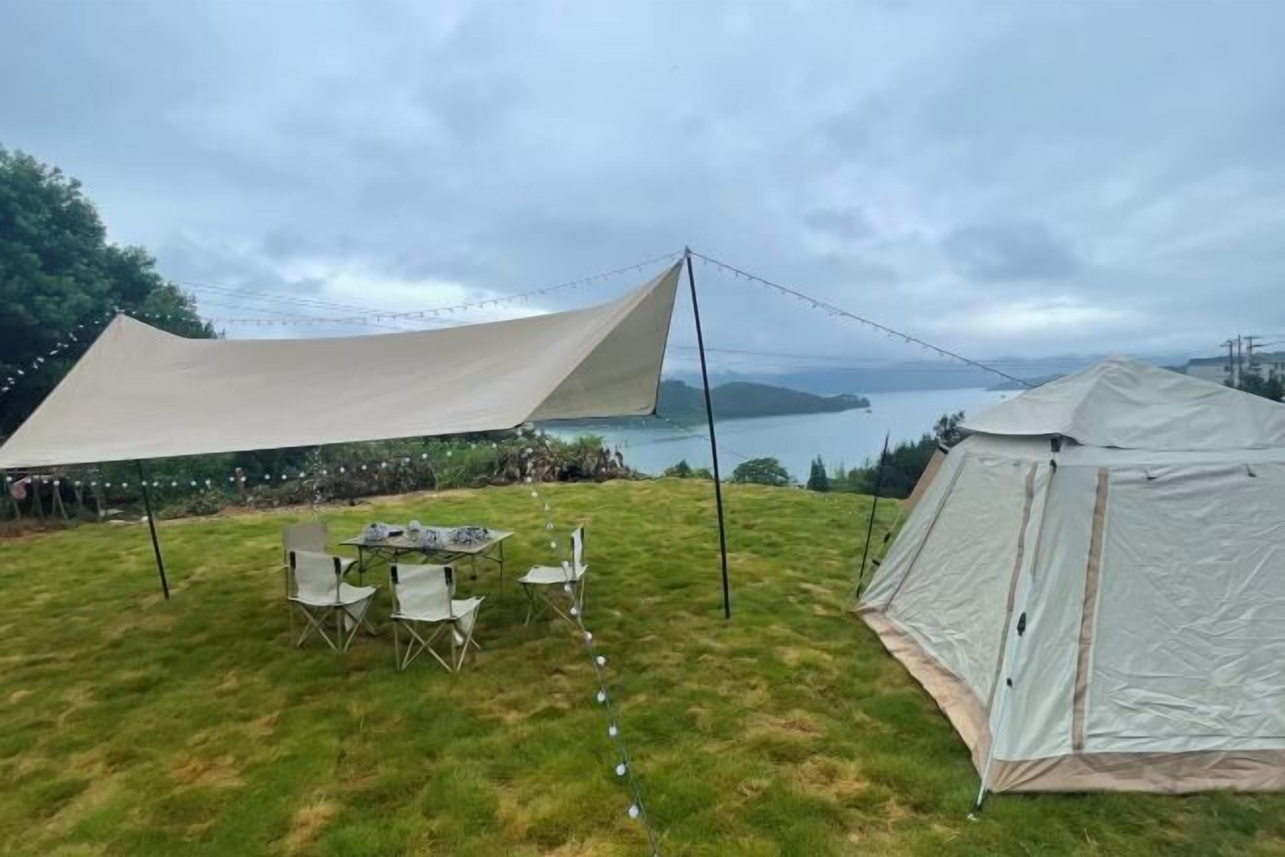 A tent set up on a grassy area with a table and chairs, overlooking a body of water.