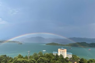 Vista costera con un arcoíris, un edificio de varios pisos y barcos en el agua.